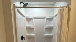 Une douche à l’italienne avec un intérieur blanc, une poignée de porte noire et un pommeau de douche.