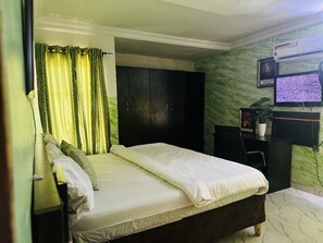 Une chambre à coucher avec un lit, une armoire sombre, un bureau avec un ordinateur et un téléviseur fixé au mur.