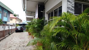 A narrow alleyway with a paved path, a parked car, and lush green plants. - The Autograph Basics Hotel (Lagos)
