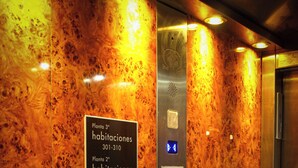 Een liftinterieur met een bord waarop plattegronden en faciliteiten staan aangegeven, zoals een receptie, parkeerplaats en een specifieke kamer genaamd 'Salón Anthed'.