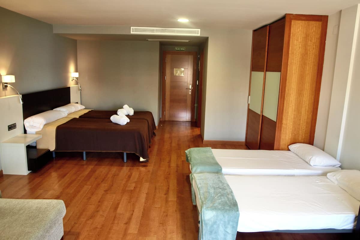 Habitación de hotel con dos camas, un armario, un escritorio y un banco.