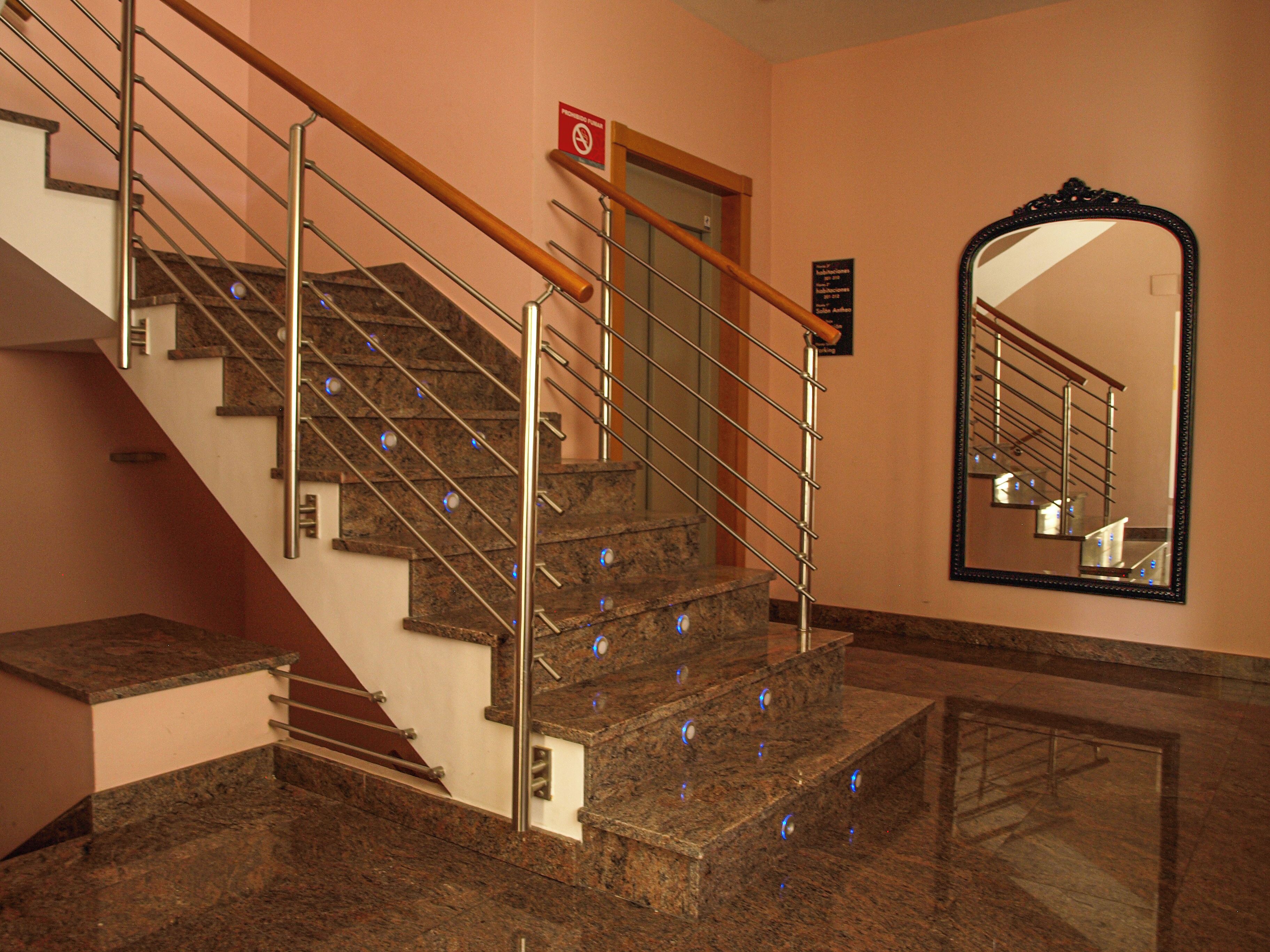 A marble staircase with metal railings and a wooden handrail, leading to a door with a no-smoking sign.