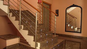 A marble staircase with metal railings and a wooden handrail, leading to a door with a no-smoking sign.