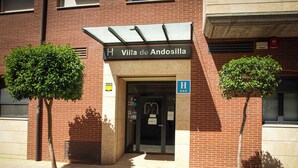 De ingang van Villa de Andosilla, een hotel met een bakstenen gevel, een overdekte oprit en twee bomen ervoor.