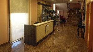 Een hotel receptie met een receptiebalie, een trap en een kamerplant.