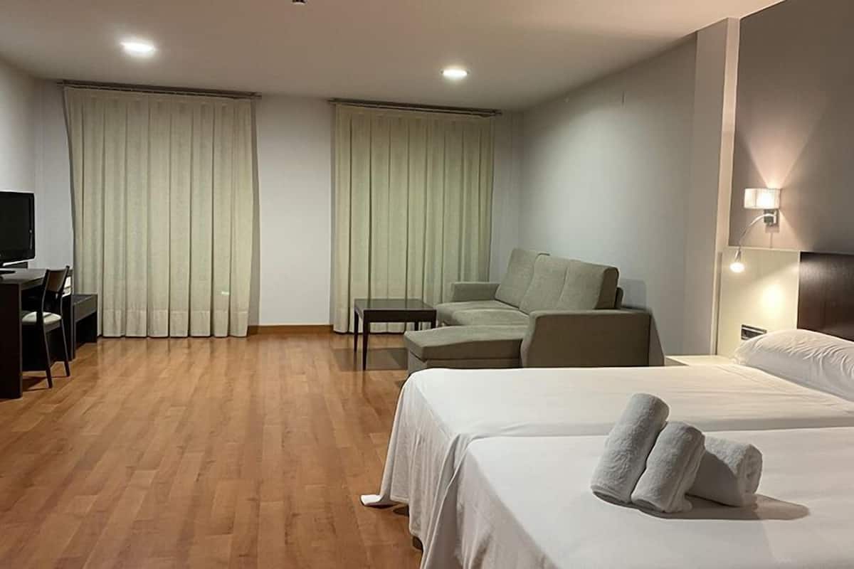 Una habitación de hotel con cama, sofá, escritorio y silla, además de cortinas.