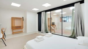 Et moderne hotelværelse med en stor seng, et træsidebord, en stol og udsigt gennem en glasdør.