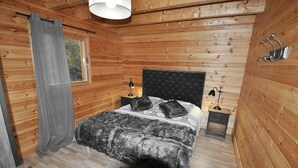 Une chambre à coucher aux murs lambrissés, comprenant un lit, deux tables de chevet, une lampe et une fenêtre avec des rideaux.