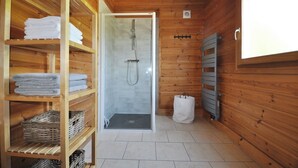 Une salle de bain rustique, avec une cabine en bois, une douche vitrée, des étagères pour les serviettes et un radiateur.