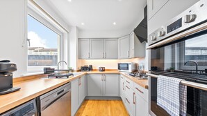 A modern kitchen with grey cabinets, a wooden countertop, a built-in dishwasher, a microwave, and a large oven. - Gateway to all of Scotland (Scone)