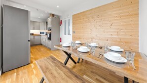 A modern kitchen with wooden flooring, a dining table set with plates, glasses, and cutlery, and a wooden accent wall. - Gateway to all of Scotland (Scone)