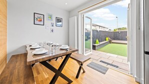 A dining area with a wooden table set for four, a bench, and a view of a backyard with a lawn and a wooden fence. - Gateway to all of Scotland (Scone)