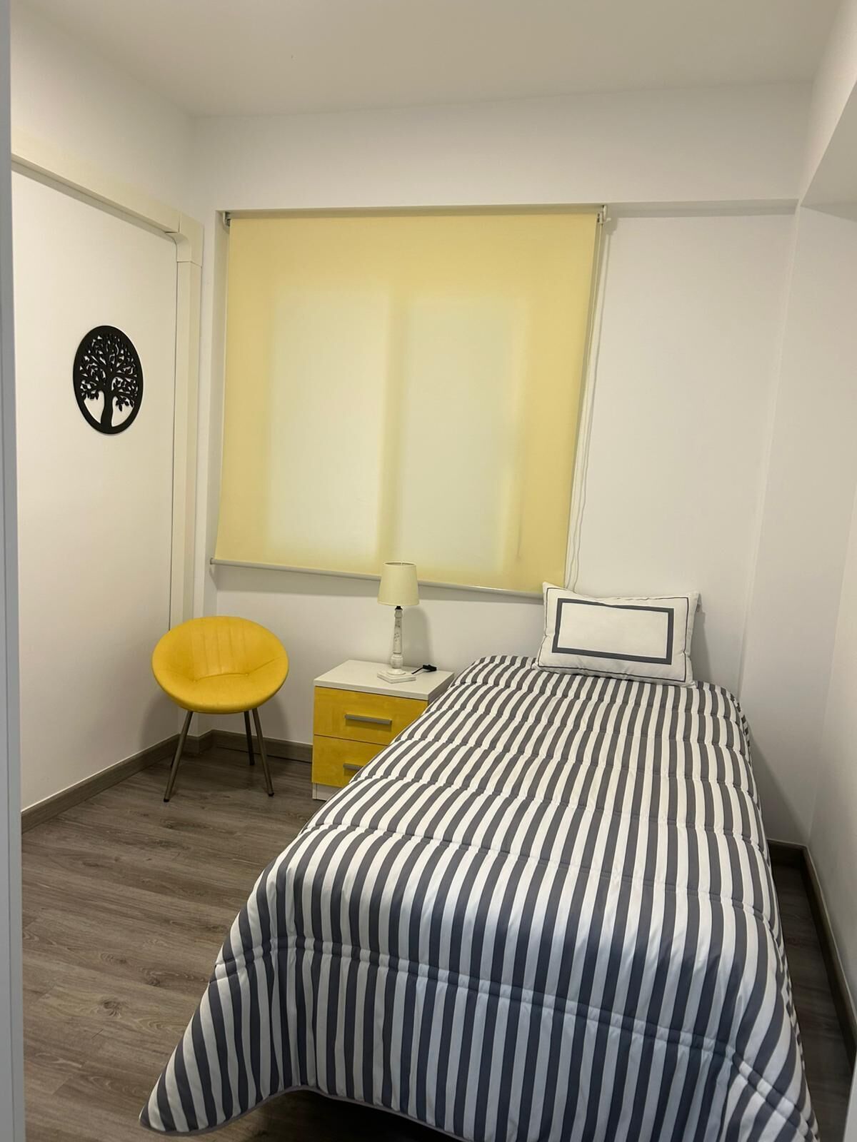 Une chambre à coucher comprenant un lit, une chaise, une table de chevet, une lampe et une fenêtre avec des stores.