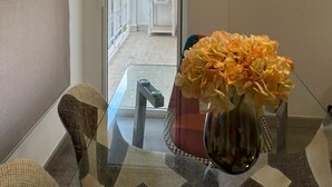 A dining area with a glass table, chairs, and a vase of flowers. There is a balcony with a white chair and a small table. - Holiday apartment Vinaròs beach vacations (Vinaròs)