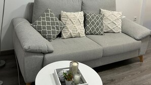 A grey sofa with patterned cushions, a framed seascape painting, a round mirror, and a small white table with a tray of decorative items. - Holiday apartment Vinaròs beach vacations (Vinaròs)