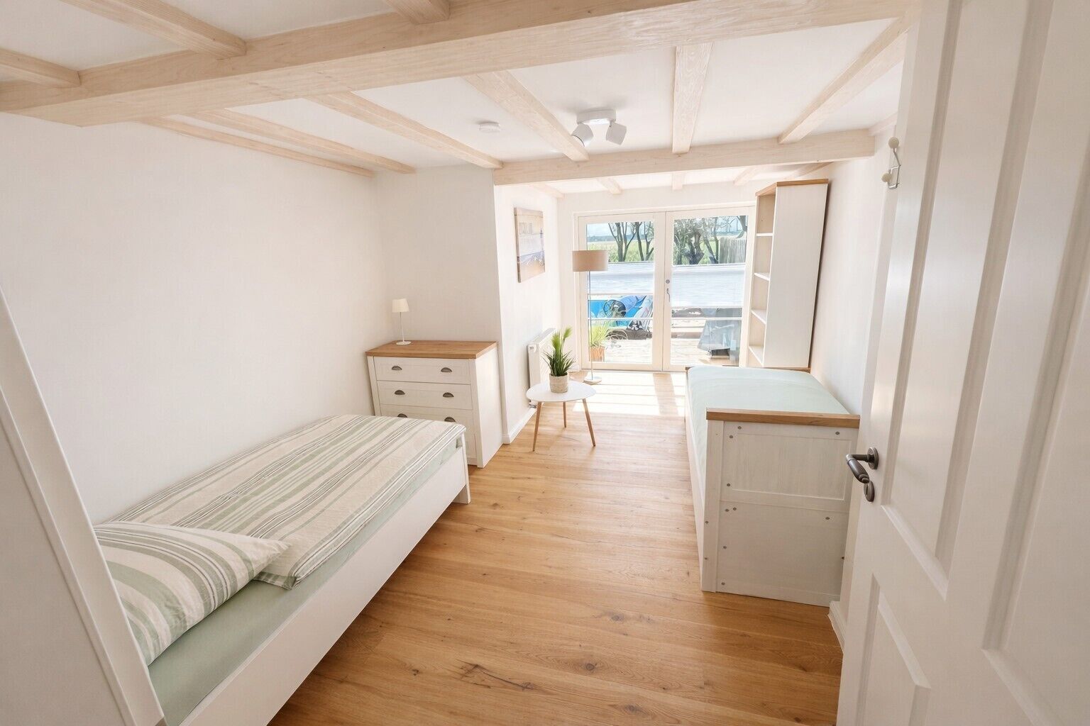 Ein schmales Zimmer mit einem Bett, einem kleinen Schreibtisch, einem Stuhl und Blick ins Freie.