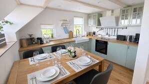 A modern kitchen with a dining area, wooden beams, and light blue cabinets. - Holiday Home 'Ferienhaus 'Huus Ant Diek Mit Pool'' with Private Pool, Private Terrace and Wi-Fi (Norden)
