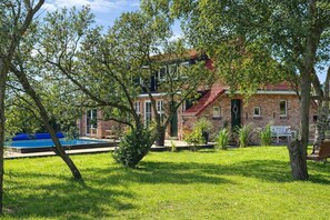 Una casa de ladrillo con techo rojo, piscina y césped bien cuidado.