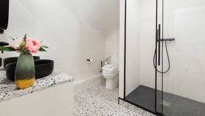 Une salle de bain moderne avec une douche à parois de verre, des toilettes blanches et un plan de toilette en marbre agrémenté d’un vase de fleurs.