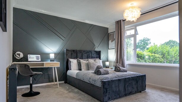 Ein Schlafzimmer mit Bett, Schreibtisch, Stuhl und einem Fenster mit Blick auf Grünflächen.
