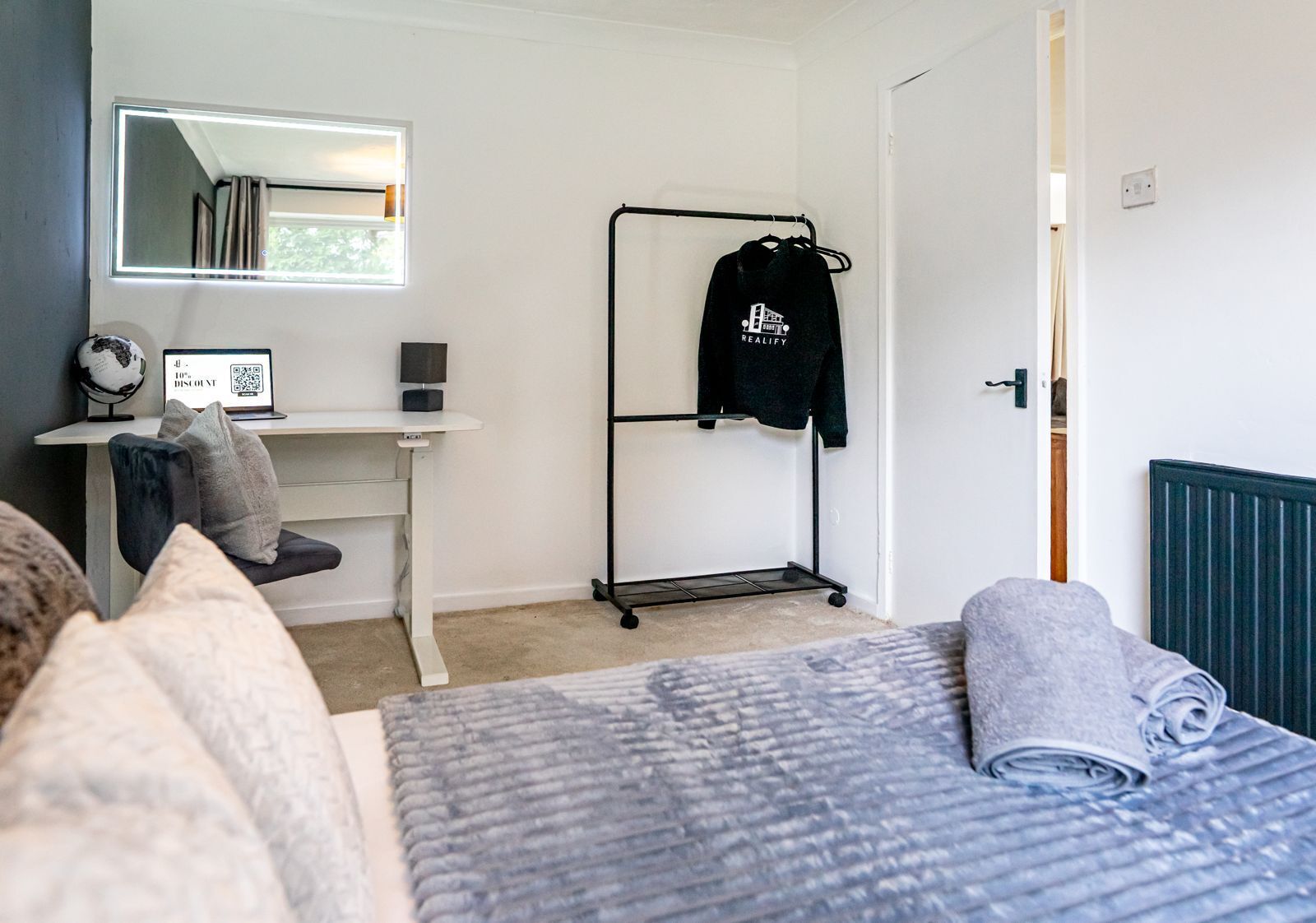 A bedroom with a bed, a desk, a chair, a wardrobe, and a hanging rack.