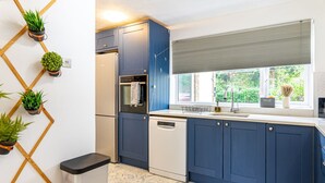 Eine moderne Küche mit blauen Schränken, einem Geschirrspüler, einem Backofen und einem Fenster mit Blick auf Grünflächen.