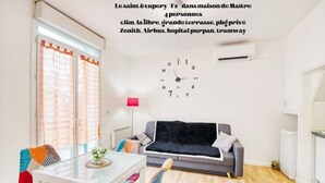 Una sala de estar moderna con una mesa de vidrio, sillas coloridas, un sofá gris y una manta negra.
