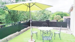 Un patio con una mesa y sillas, un paraguas amarillo y un césped verde.