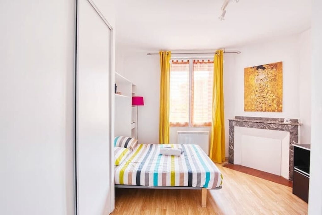 Une petite pièce lumineuse, avec un lit, un radiateur, une petite table et un tableau accroché au mur.