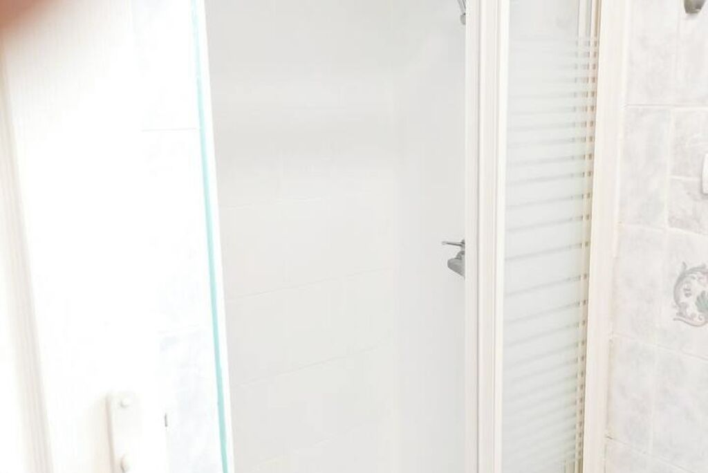 Un baño con cabina de ducha de vidrio, pared con azulejos blancos y ducha.