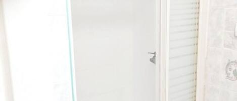 Un baño con cabina de ducha de vidrio, pared con azulejos blancos y ducha.