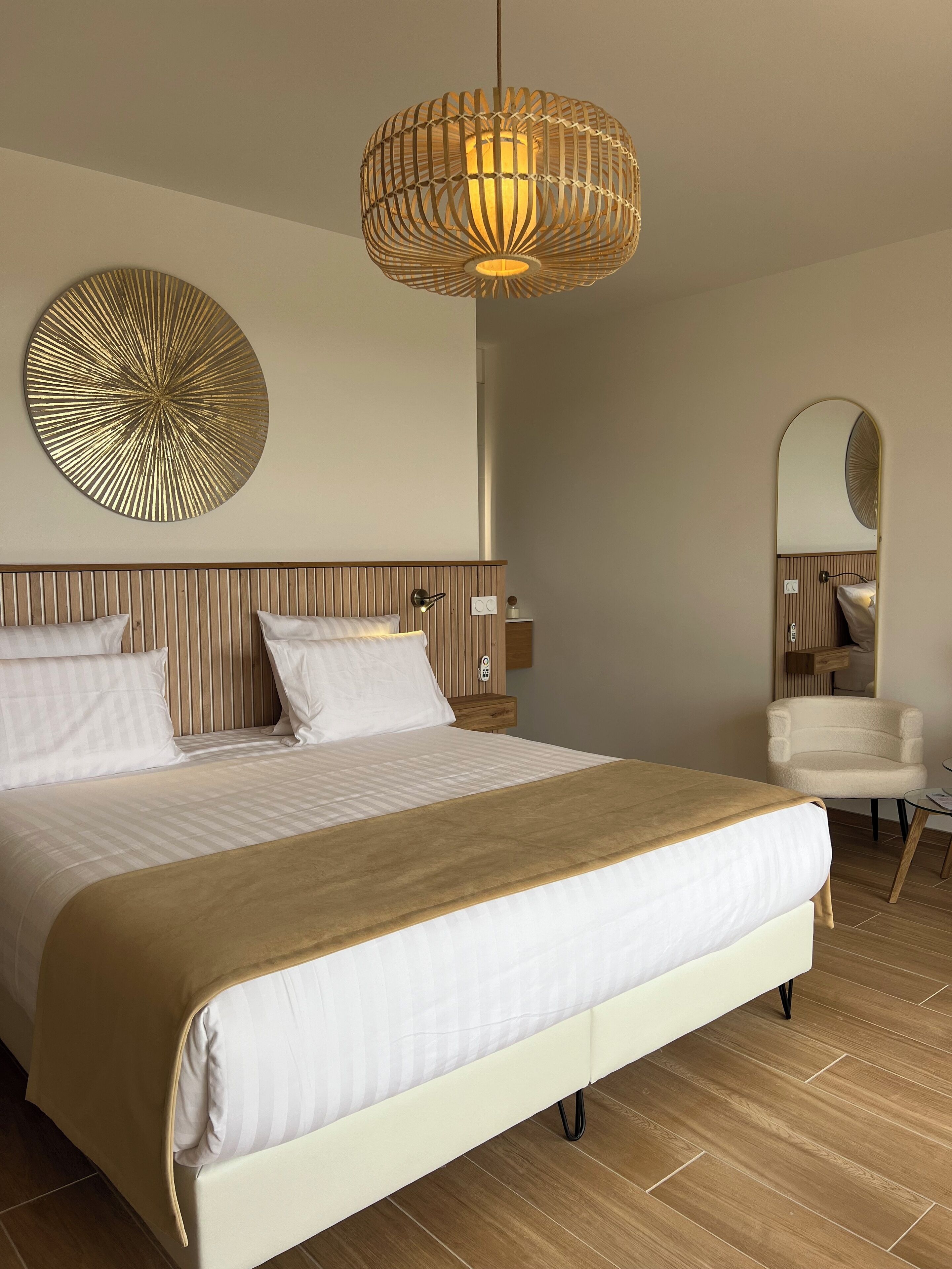Un dormitorio moderno con una cama grande, una lámpara colgante, un adorno circular en la pared, una silla y un espejo.