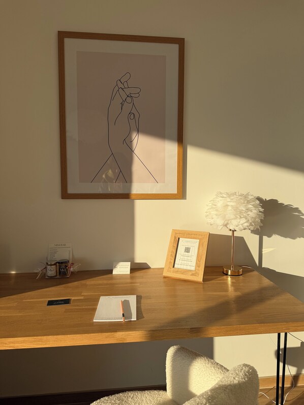A wooden desk with a framed abstract artwork, a small framed certificate, a decorative lamp, and a white chair.