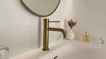 A bathroom with a white bathtub, a gold faucet, a round mirror, and a towel with a red flower.