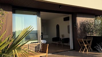 A modern house with a patio area featuring wooden furniture and a view of the interior.