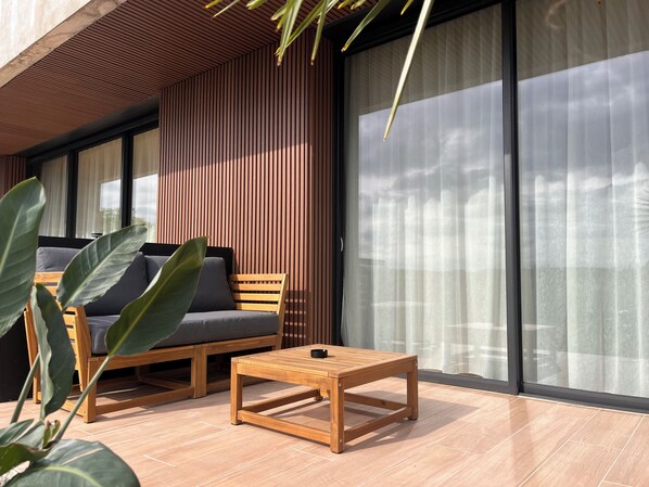 A modern outdoor seating area with a wooden table and chairs, a large plant, and a sliding glass door.