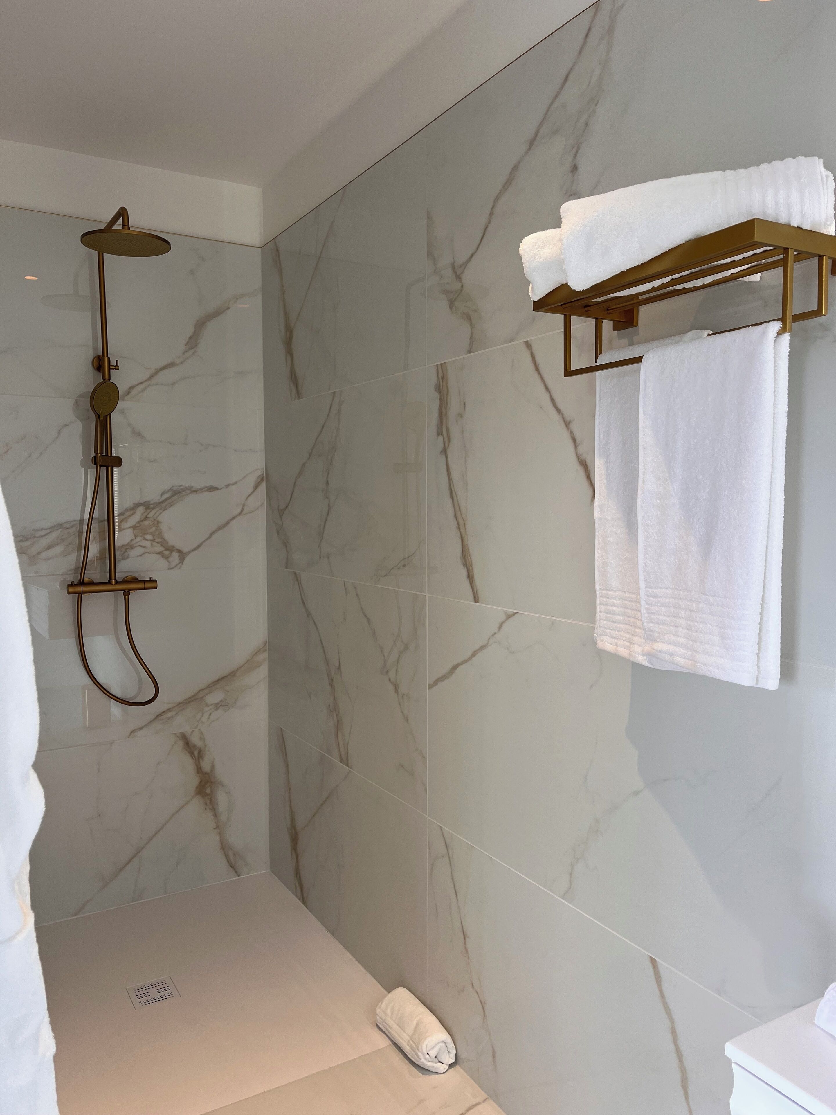 Une salle de bain moderne avec une douche, des murs en marbre et un porte-serviettes.