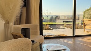 Un salon moderne avec un canapé, une table basse en verre et une vue sur un jardin, accessible par une porte-fenêtre coulissante.