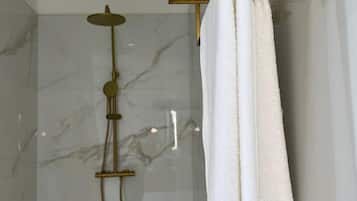 A modern bathroom with a marble shower wall, a gold showerhead, and white towels hanging on a gold towel rack.