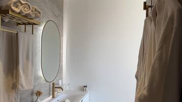 A modern bathroom with a marble wall, a gold-framed mirror, a white vanity, and a towel rack.