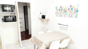 Una habitación pequeña y luminosa con una mesa de comedor, dos sillas, un microondas y una cafetera.