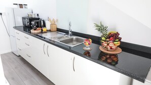Una cucina moderna con un piano di lavoro nero, mobili bianchi, un lavello in acciaio inossidabile, una macchina da caffè, un tostapane e una ciotola di frutta.