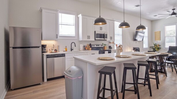 A modern kitchen with white cabinets, stainless steel appliances, and a central island with bar stools. - Walk to Riverwalk! 3BR/2BA Gem Near Fun Downtown! (San Antonio)