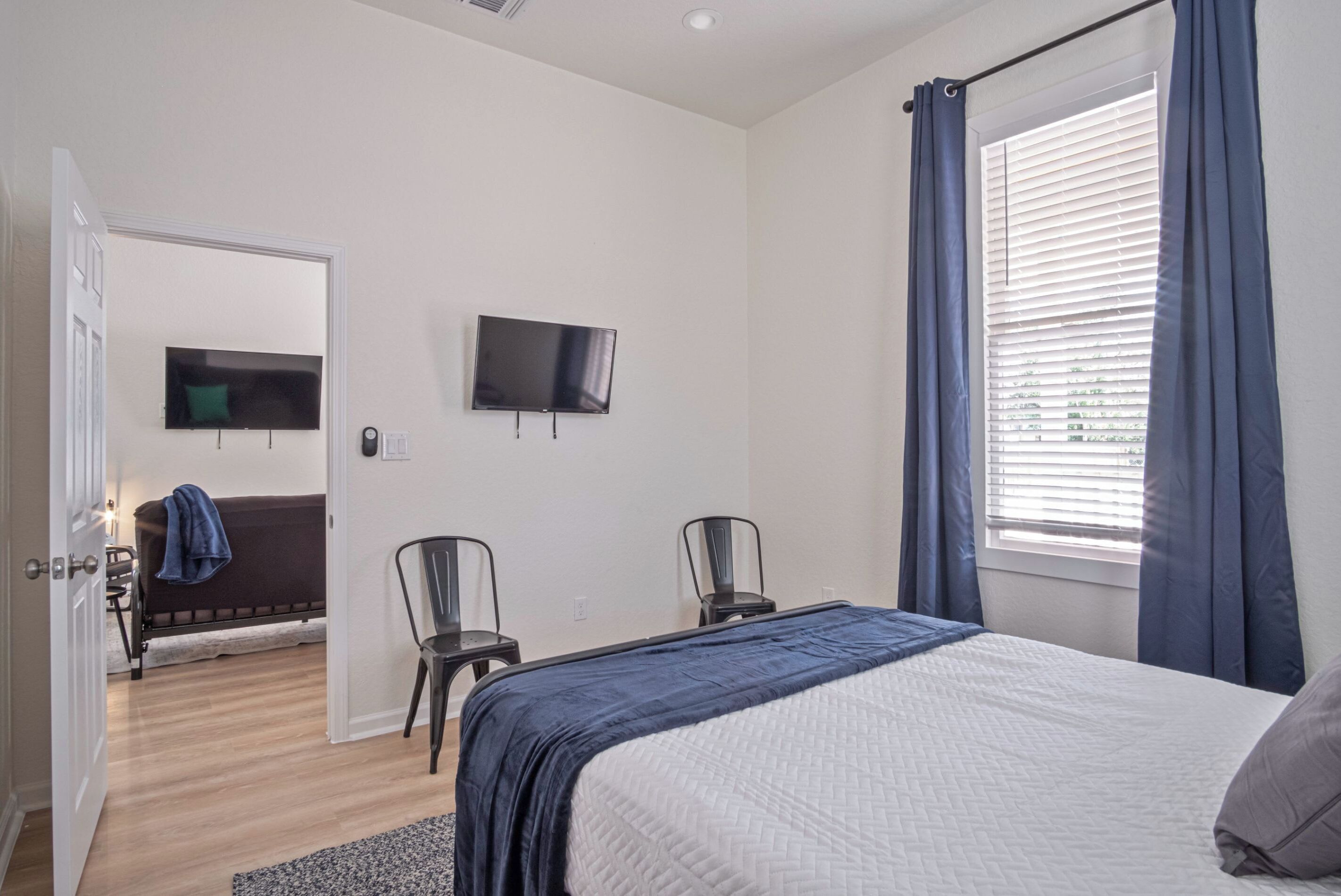 A bedroom with a bed, two chairs, a TV, and a window with curtains.
