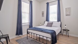 A bedroom with a bed, two windows with curtains, a bedside table, and a wall-mounted TV. - Walk to Riverwalk! 3BR/2BA Gem Near Fun Downtown! (San Antonio)