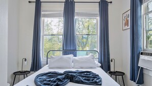 A neatly made bed with a remote control, a blue blanket, and a white pillow. There are two bedside tables with lamps.