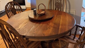 Un coin repas avec une table en bois, des chaises, une horloge et des appareils de cuisine en arrière-plan.