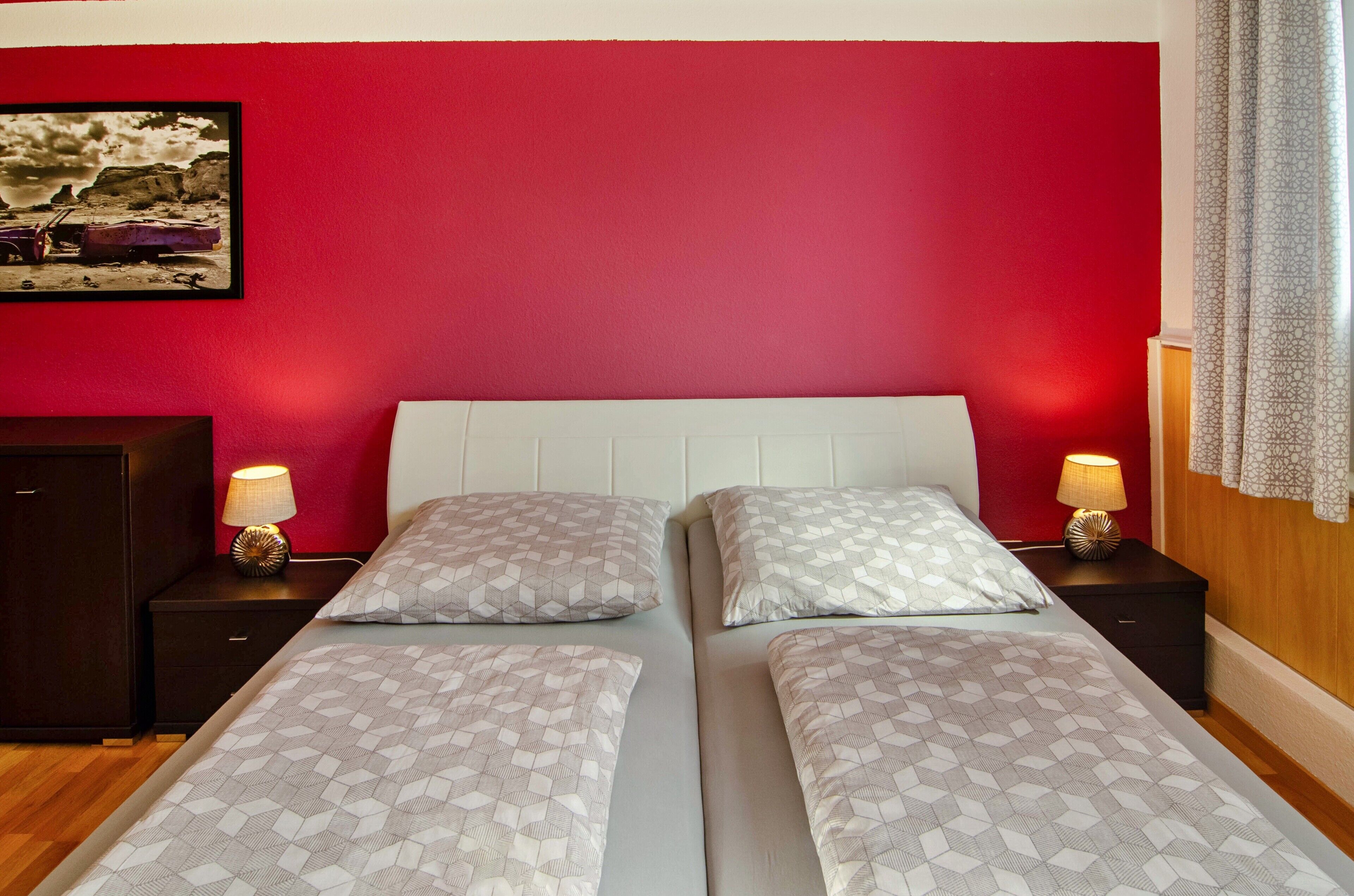 Een tweepersoonsbed met beddengoed met patroon, twee bedlampjes en een rode accentmuur.