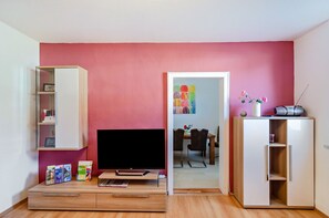 A living room with a flat-screen TV, a bookshelf, a cabinet, and a dining area in the background. - Holiday Apartment 'Gräfe' (Herzberg am Harz)