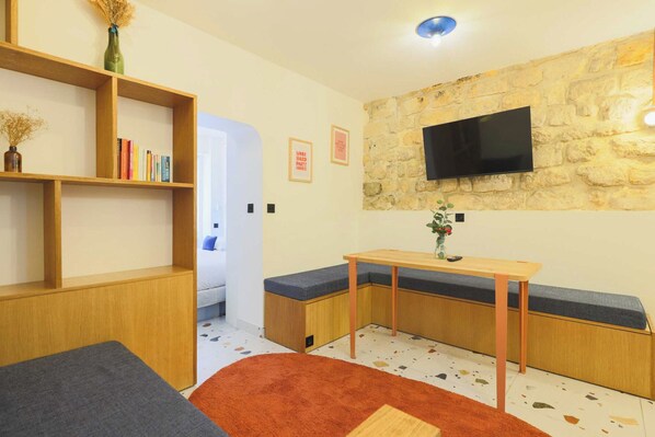 Une pièce moderne avec une bibliothèque en bois, un téléviseur fixé sur un mur en pierre, une petite table en bois et un banc avec des coussins.